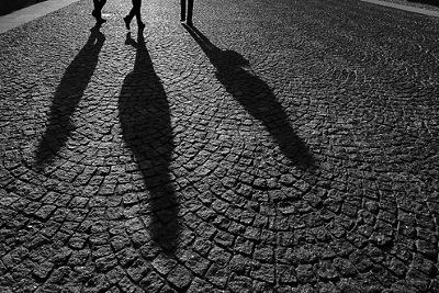 Black and white image three people's shadows stretched out across a cobblestoned road
