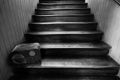 Black and white image of old wooden stairs with an old radio perched on the bottom step