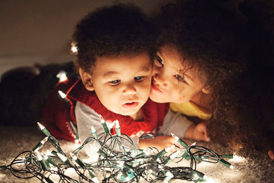 two children lying on carpet with white Christmas lights illuminating their faces