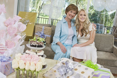 bride to be and her mother sitting together on a couch surrounded by gifts, flowers, and desserts