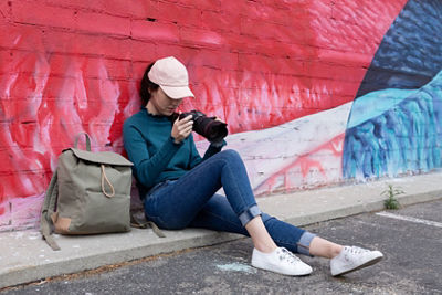 A woman sits against a colorful wall looking at her camera
