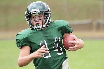 Middle school football player running with the ball tucked under left arm