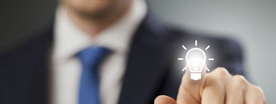 A man in a suit putting his finger forward and placing it on a lightbulb. 