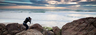 A woman uses a camera on a tripod to take a photograph of the ocean