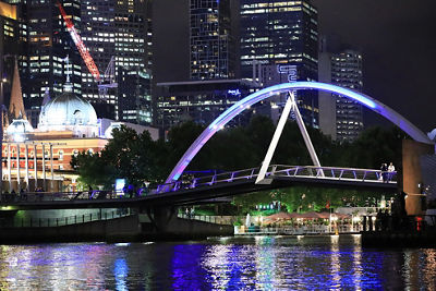 Nighttime action shot of a purple illuminated bridge and sky screapers in the background