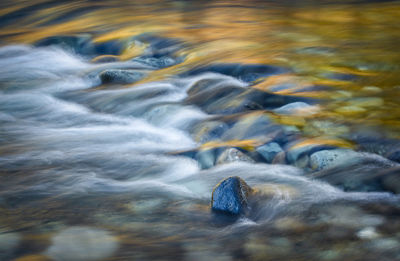 Close up image on smooth blue and neutral colored stones in a river with the water flowing softly over the bumps and divets the stones create