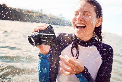 Woman in ocean with camcorder laughing