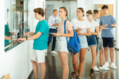 Teenage students queuing at front office on college campus.