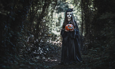 Girl in spooky costume holding a jack-o-lantern