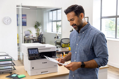 Person Holding Paper Next to a Canon Printer