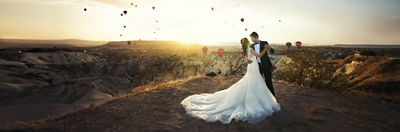 Bride and Groom standing on a mountaintop with hot air balloons and other mountains in the background