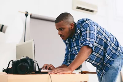 A man is leaning over a desk looking at a laptop