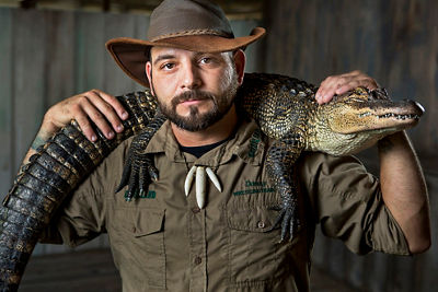 A man with an australian exploratory cap holding an alligator crested on his shoulders