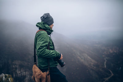A person holds a camera while standing on top of a mountain