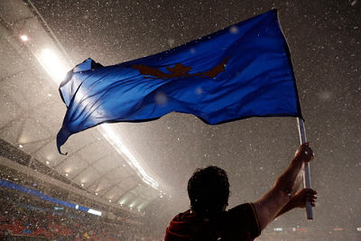 Soccer action shot - player waving a large blue flag as it snows in the stadium