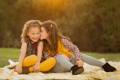 two girls sitting on a blanket in field