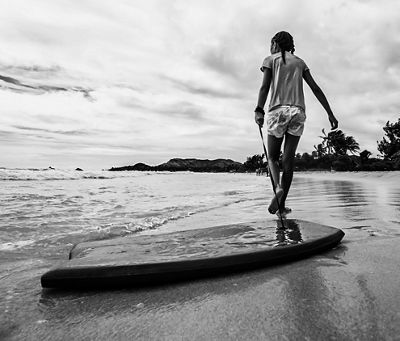 Black and white ground shot of Laura's daughter walking down the beach with her board