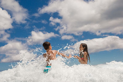 Laura's kids playing in the waves with the blue sky behind them