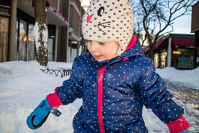 Young girl in blue polka dot parka and cat snow hat looking away from the camera