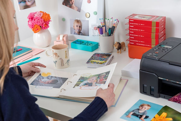 Personne à un bureau regardant un album photo près d'une imprimante Canon et de fournitures.