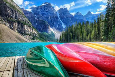Canoes on a lakeside dock in front of a forest and mountains