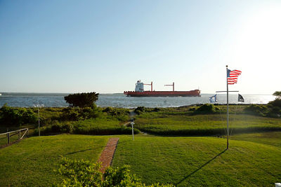 Crisp photo of golf course photo with american flag overlooking water with large boat