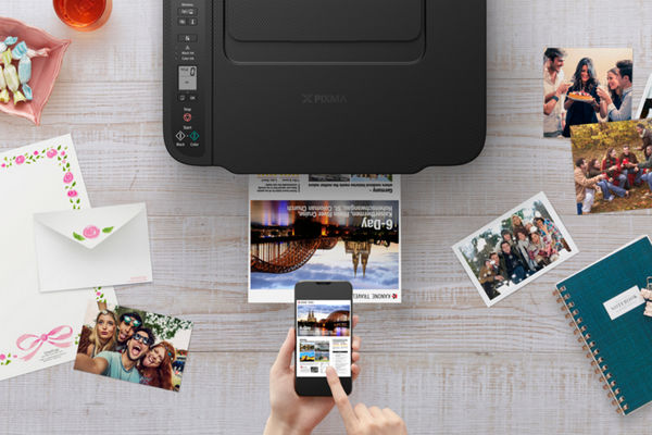 Person printing photo from phone using PIXMA printer on wooden table.