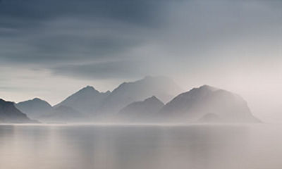 Gloomy mountains across a body of water with fog