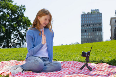 Person Sitting on a Blanket in a Park Waving to a Camera