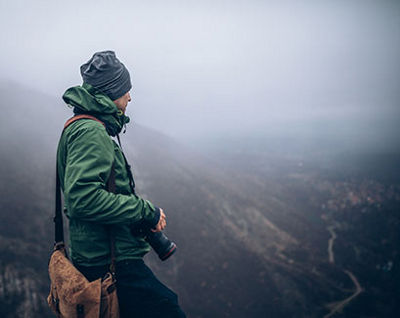 A man holds a camera while looking out from the top of a mountain. The image has a red overlay