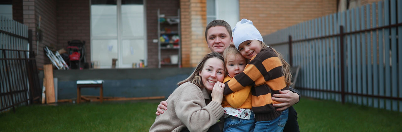 Mother, father and two sibling sisters together near house in autumn in warm sweaters.Portrait of family enjoying free time outdoors. Happy family with two children on backyard of their brick townhouse.