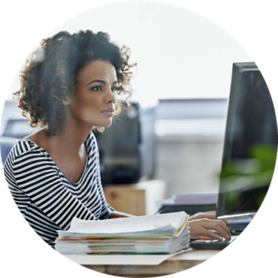 Woman working at desk and computer with stack of papers