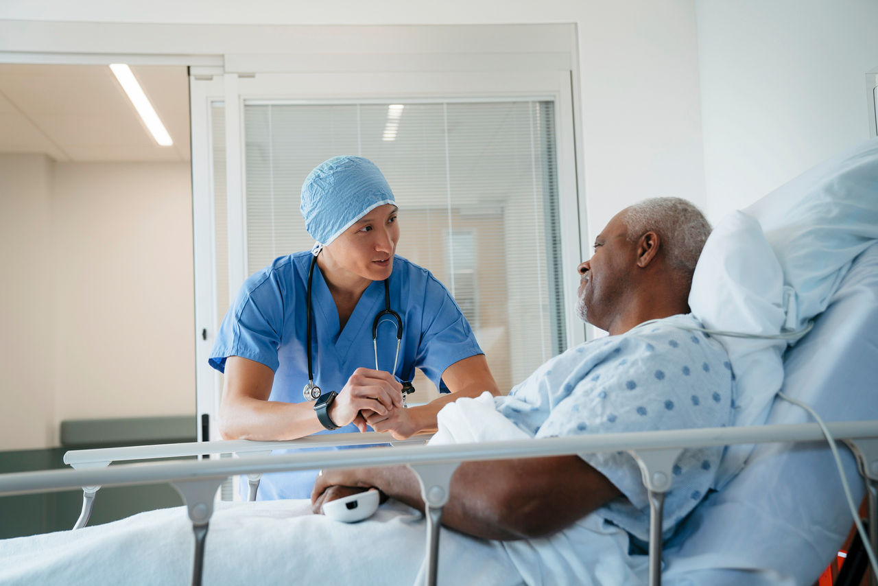 Surgeon talking with senior patient lying on bed in hospital ward