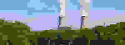 Two cooling towers with water vapor behind a bridge and trees