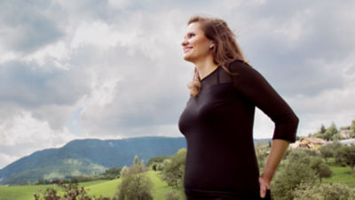 A woman from the waist up, standing outside and smiling into the distance, with mountains in the background. 