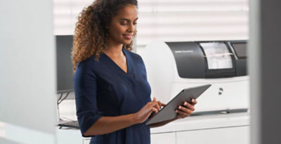 Dental professional using a tablet to access CEREC on DS Core with in-house manufacturing units in the background.
