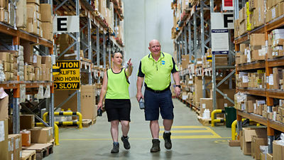 Two warehouse professionals walking toward camera through an aisle.