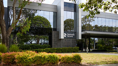 Front of Dentsply Sirona office building with trees and hedges in foreground.