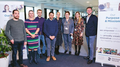 Eight professionals from Dentsply Sirona standing in front of company mission and values signage.