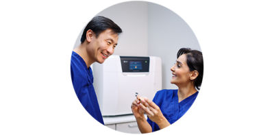 Dental professional holding an aligner while consulting with a patient near an intraoral scanner.