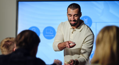 Male clinician teaching implant techniques to a seated group.