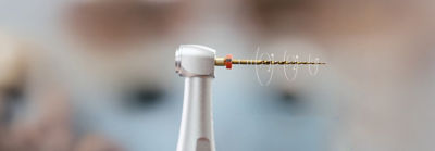 Close-up of a dental handpiece with a reciprocating file attached, positioned for endodontic use.