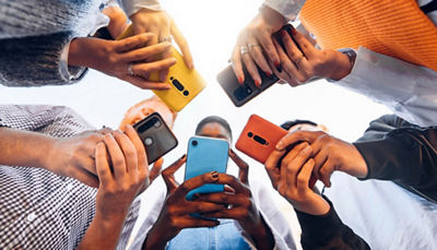 Low-angle view of a group of people standing in a circle, holding colorful smartphones.