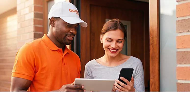 A Boost Mobile delivery driver helping a smiling customer set up a new smartphone at her door.
