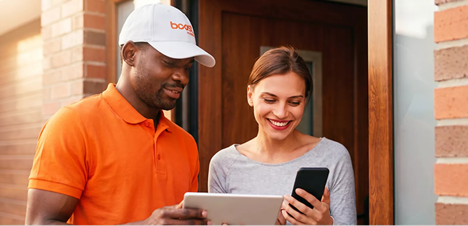 A Boost Mobile delivery driver helping a smiling customer set up a new smartphone at her door.