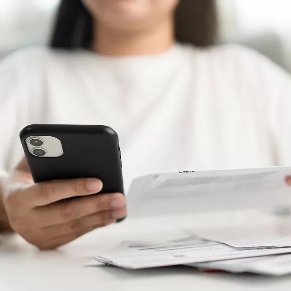 A person holding a black smartphone in one hand while reviewing a paper bill in the other.
