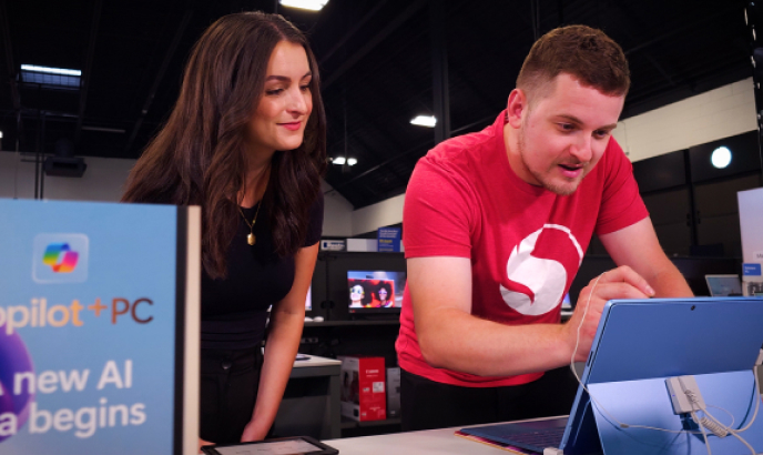 Two people stand at a PC display inside of a tech retailer.