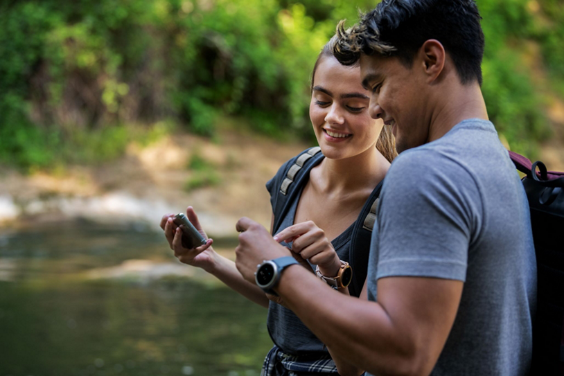 A couple use a generative AI device while hiking outdoors.