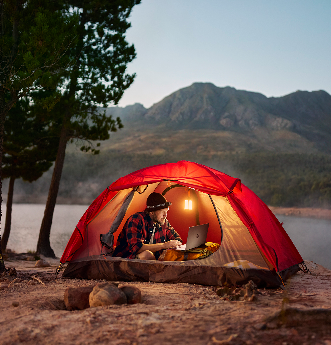 Man camping by a river with a laptop.