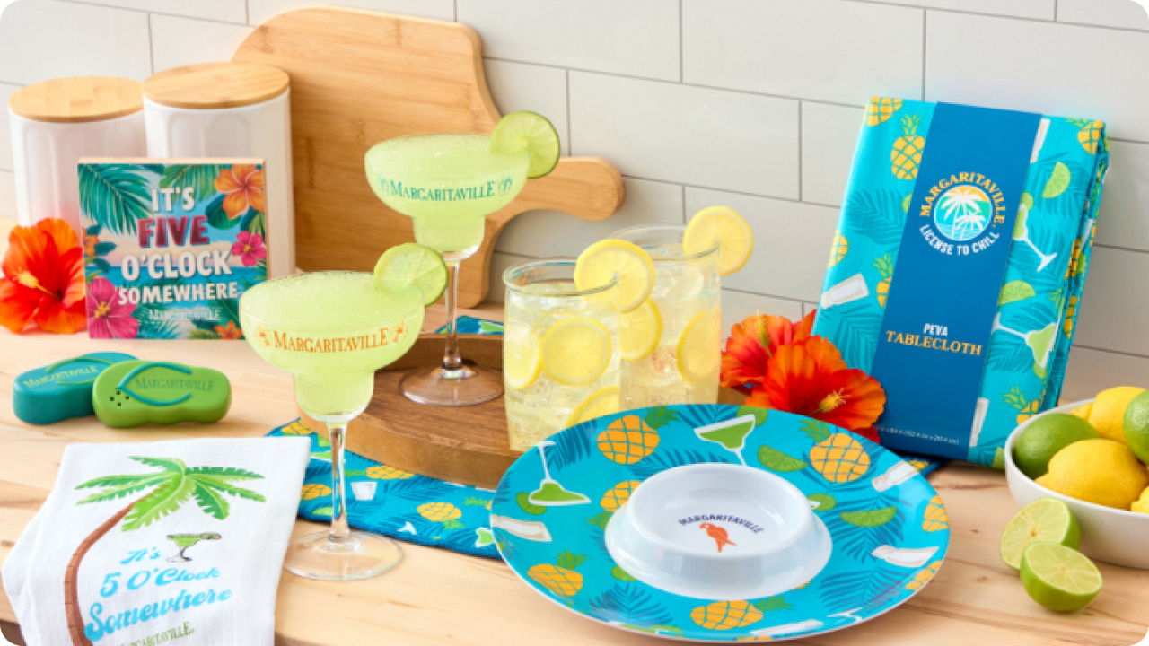 Margaritaville margarita party set with lime margarita glasses, tropical pineapple plates, cocktail napkins, coasters, and décor arranged on a kitchen counter, styled for summer entertaining.